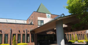 赤レンガ造りの介護施設建物外観。緑色の屋根と木製の庭園施設が見える。